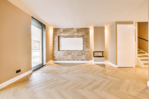 General view of an empty bright room with a large window and a small fireplace on a parquet floor of a modern house