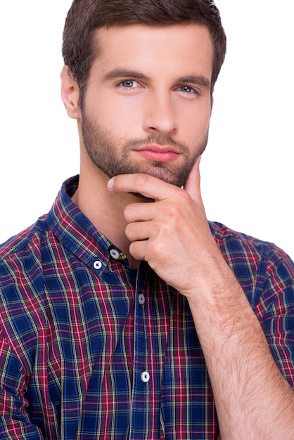 Generating fresh ideas. Portrait of thoughtful young man in casual shirt holding hand on chin and looking at camera while standing isolated on white