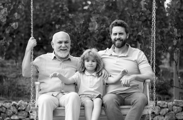 Generations family grandfather with son and grandson on a swing in spring garden outdoors active