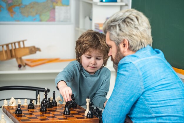 Generations men cute little boy playing chess with parents nice concentrated little boy sitting at t...