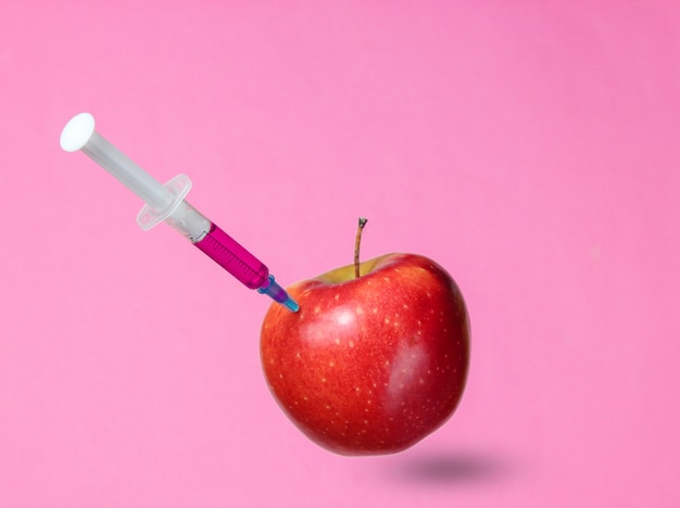 Генетически модифицированное красное яблоко со шприцами на розовом