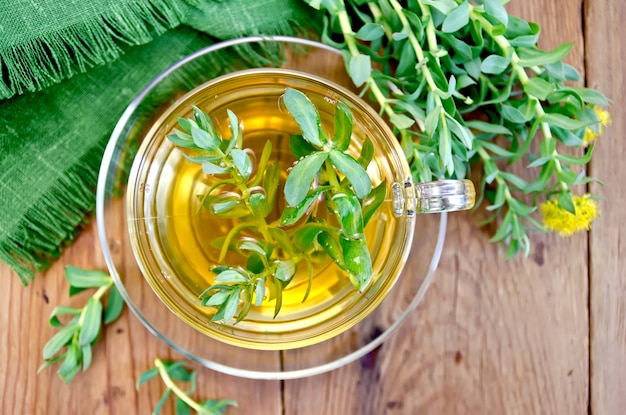 Genezende kruidenthee in glazen beker met bloemen Rhodiola rosea, groene doek op een houten plank erop