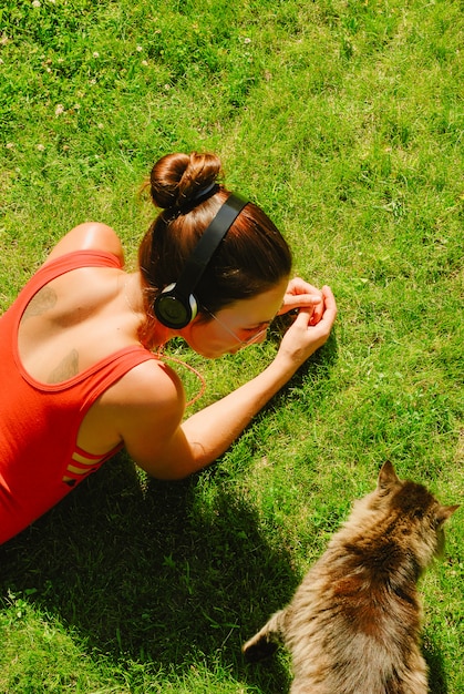 Foto geniet van de muziek, bovenaanzicht van jonge brunette vrouw in rood shirt, koptelefoon dragen, kijken naar kat