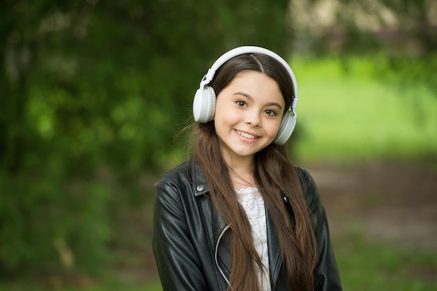 Geniet van geluidsmuziek Gelukkig kind luistert naar de soundtrack in het park Klein meisje geniet van muziek in oortelefoons HiFi-stereogeluid Nieuwe technologie Modern leven Perfecte dag heeft perfect geluid nodig