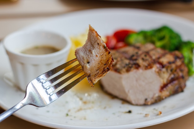 Geniet van het eten van hapje van sappige biefstuk met vork en wazige achtergrond