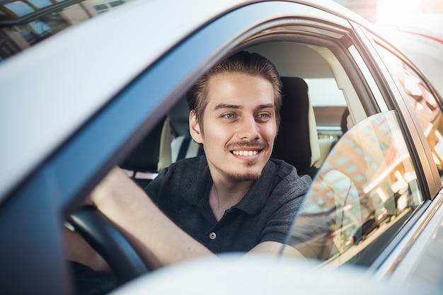 Geniet van het rijden. Afbeelding van een jonge knappe jongen die in de auto zit.