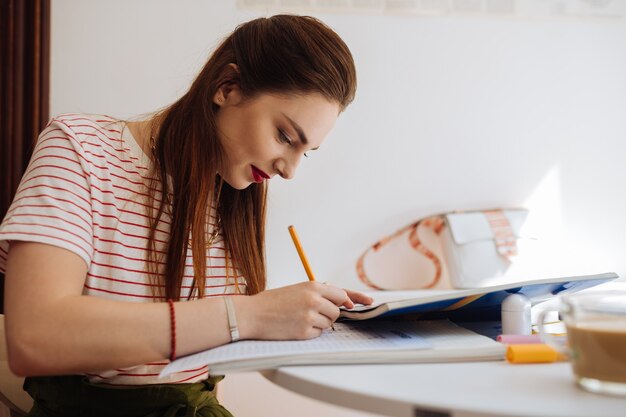 Geniet van je studie. Leuke student die glimlach op haar gezicht houdt tijdens het voltooien van de test