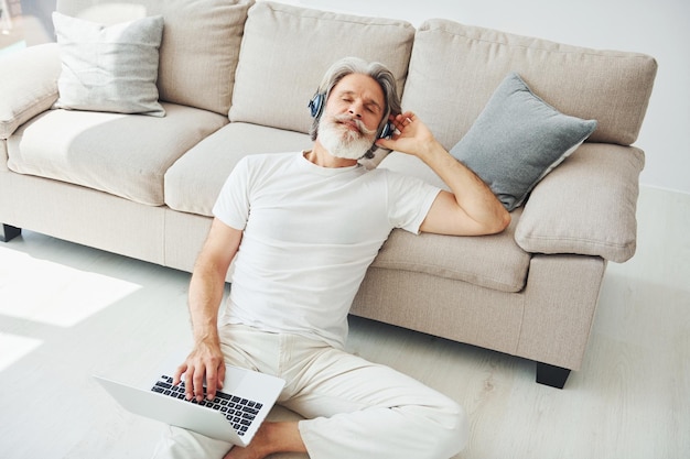 Geniet van muziek Senior stijlvolle moderne man met grijs haar en baard binnenshuis