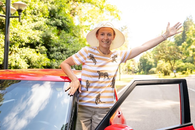 Genieten van aankoop bij dealer, huur een auto, reisconcept, positief vrolijk meisje, funky bestuurder, geniet van hits, vrolijke jonge vrouw is in de buurt van glanzende rode auto