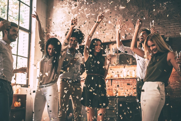 Genieten van een cool feest. Groep gelukkige jonge mensen die confetti gooien en springen terwijl ze genieten van een thuisfeest in de keuken