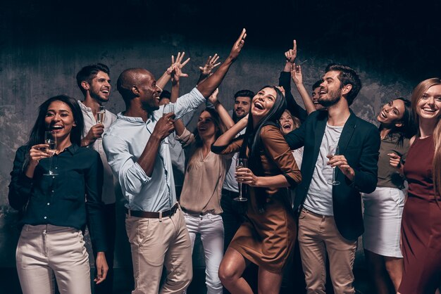 Genieten van een geweldig feest. Groep mooie jonge mensen die dansen met champagnefluiten en er gelukkig uitzien