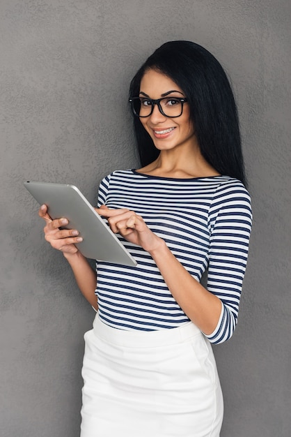 Genieten van haar nieuwe tablet. mooie jonge afrikaanse vrouw die op digitale tablet werkt en naar de camera kijkt met een glimlach terwijl ze tegen een grijze achtergrond staat