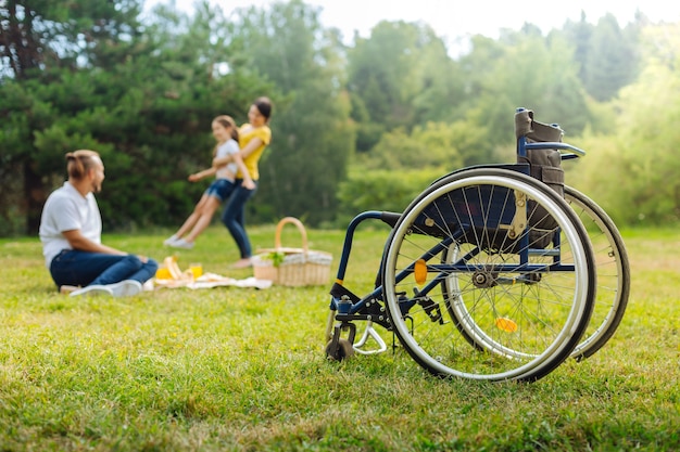 Genieten van het leven. De focus ligt op een rolstoel van een jonge man met een mobiliteitsbeperking die zijn vrouw ziet ronddraaien tijdens een picknick in het park