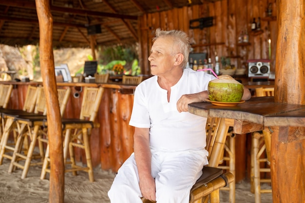 Genieten van het pensioen. Gelukkig senior man drinkt een kokosnoot water in de strandbar.