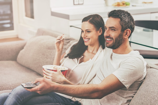 Genieten van hun favoriete show. mooie jonge verliefde paar hechten aan elkaar en eten popcorn terwijl ze op de bank zitten en tv kijken