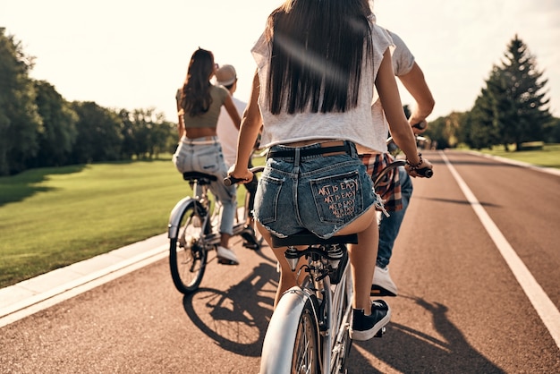 Genieten van vrijheid. Achteraanzicht van jonge mensen in vrijetijdskleding die samen fietsen terwijl ze zorgeloze tijd buitenshuis doorbrengen