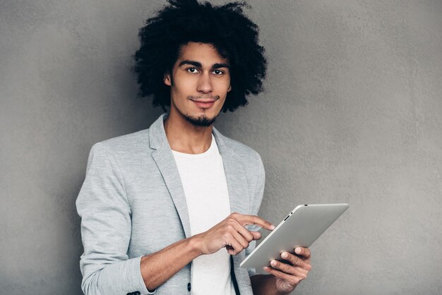 Genieten van zijn digitale tablet. Jonge Afrikaanse man aan het werk op zijn digitale tablet terwijl hij staat