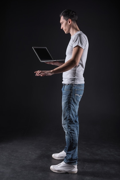 Genius programmer. Serious handsome intelligent man typing on the keyboard and holding his laptop while being a professional programmer