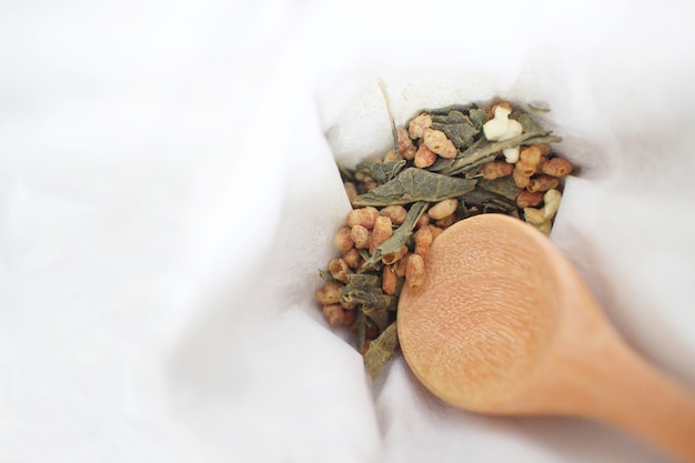 Genmaicha, a Japanese brown rice green tea consisting of dried green tea mixed with roasted popped brown rice with a wooden spoon on white fabric background