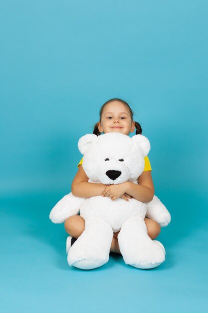 Gentle affectionate girl  sits on the floor and hugs white teddy bear