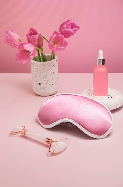 Gentle background for cosmetics product presentation with rose\
quartz massage roller sleeping mask and bottle of cosmetic oil or\
serum mock up of skin care at home