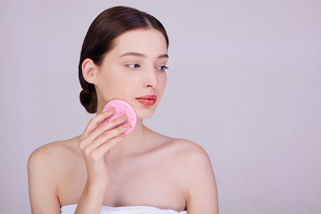 A gentle brunette cleanses her skin with a sponge.
