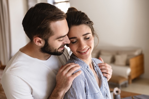 Dolce coppia bruna innamorata uomo e donna sorridente mentre abbracciano insieme in appartamento