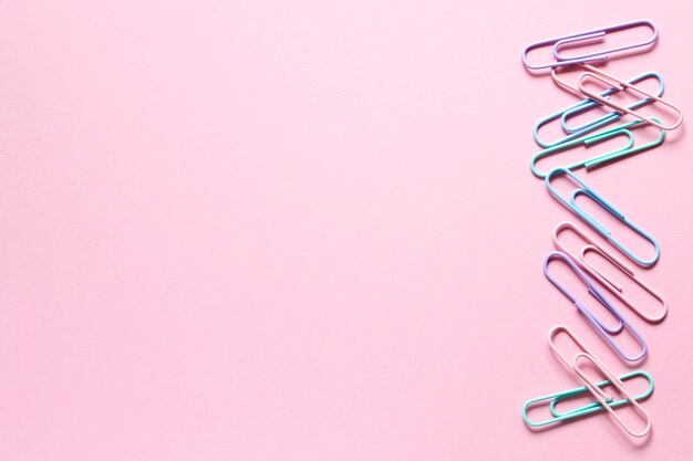 Photo gentle color paper clips laid out on a delicate pink background on one side in a row.