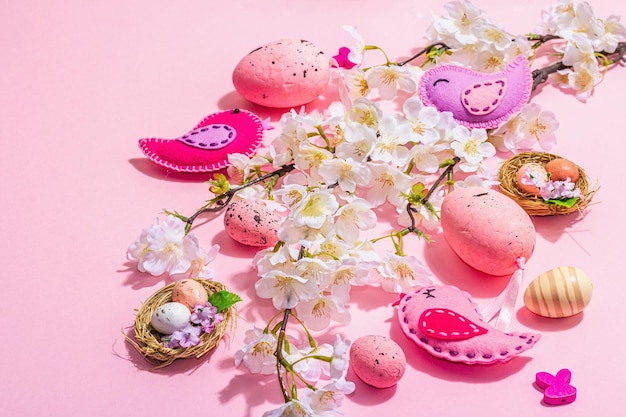 Gentle Easter composition with cherry flowers and handmade felt birds Decorative eggs and nest cute rabbits Hard light dark shadow pink background copy space