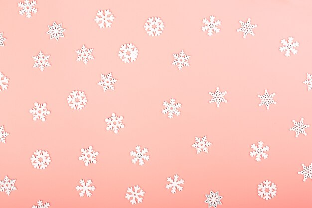 白い雪片と穏やかにピンクの冬の背景。創造的なクリスマスのレイアウト。ミニマルなスカンジナビアスタイル。テキスト、上面図、フラットレイ用の空のスペース