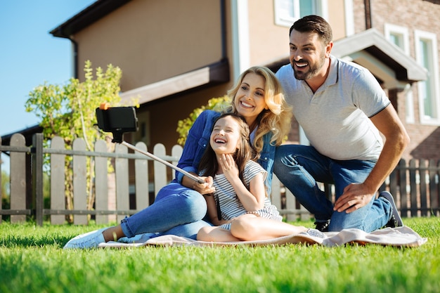 Photo genuine happiness. happy cute little girl sitting on the rug next to her father and mother and taking a selfie of her family while all of them smiling broadly