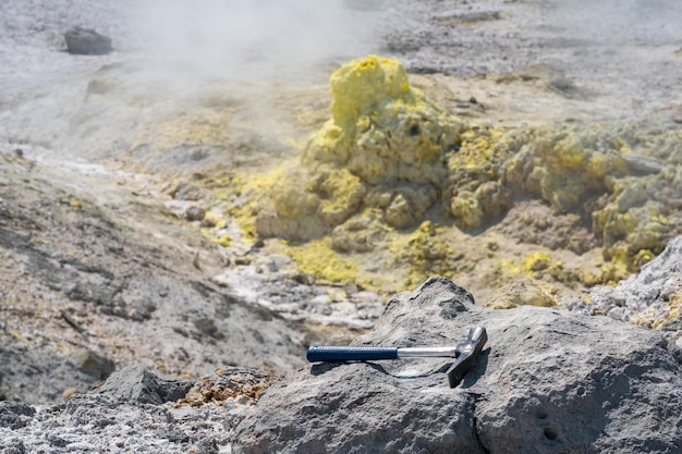 Geological hammer on the rock against the backdrop of an\
steaming fumarole on the slope of a volcano