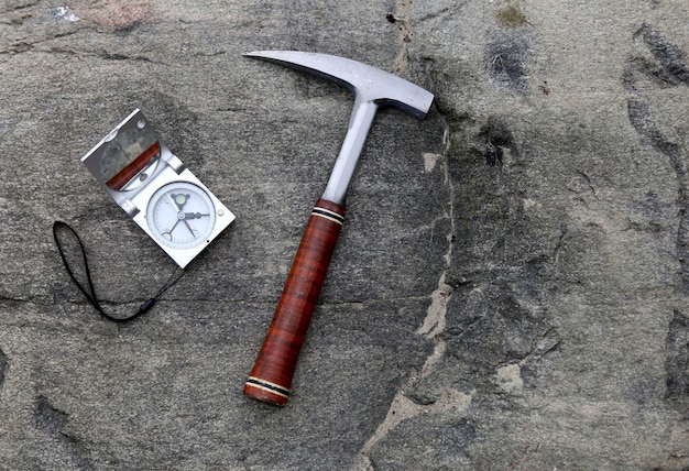 geologist compass on stones with hammer. science concept. hammer and tools are laid out on filedwork