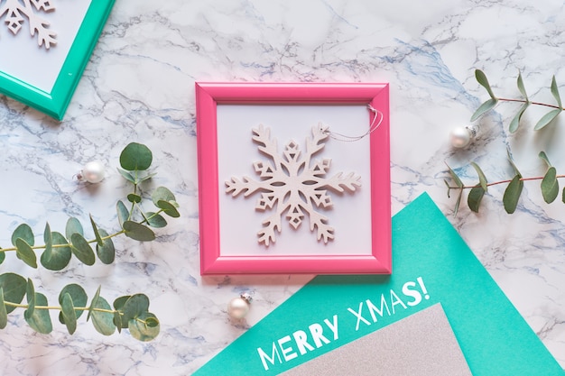 Geometric Christmas flat lay top view with pink and green frames. Fresh eucalyptus twigs and decorative white sparkling snowflake in pink frame.