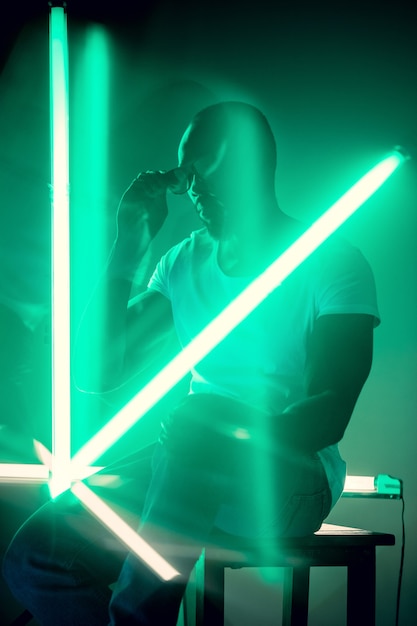 Geometric lines. Cinematic portrait of stylish young man in neon lighted room. Bright neoned colors. African-american model, musician indoors. Youth culture in party, festival style and music concept.