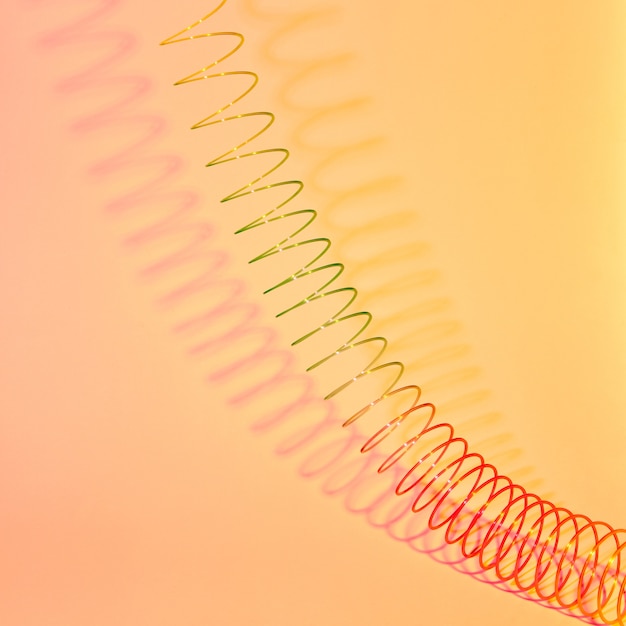 Geometrische vorm van hyperbool van het uitrekken van gekleurde plastic spiraal op een pastel gele achtergrond met zachte schaduwen, kopieer ruimte.