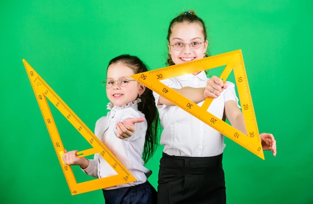 Geometry favorite subject Education and school concept School students learning geometry Kids school uniform green background STEM school disciplines Classmates cute girls with big rulers