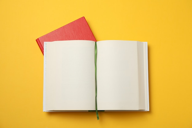 Geopend leeg boek en rood boek op gele ruimte, ruimte voor tekst