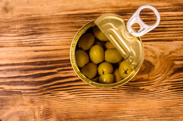 Geopende blikje met groene olijven op rustieke houten tafel. Bovenaanzicht