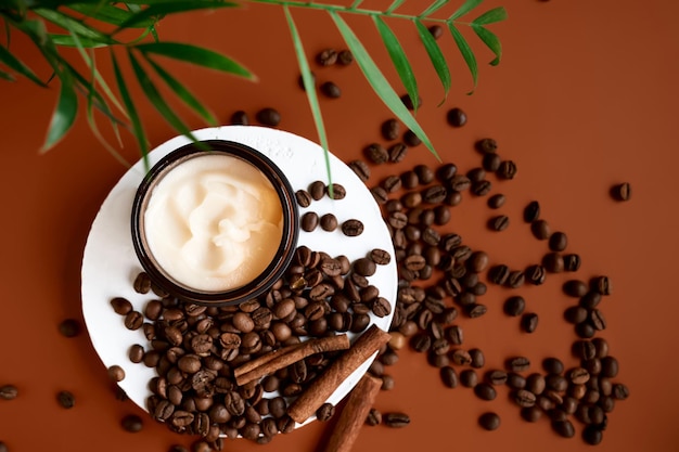 Geopende bruine zalfpot op gipscilinderpodium met palmbladeren, koffiebonen en kaneel