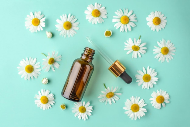 Geopende fles met een pipet en kamille bloemen op een blauwgroene achtergrond