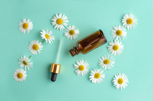 Geopende fles met een pipet en kamille bloemen op een blauwgroene achtergrond