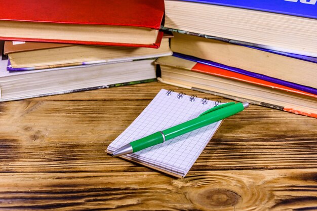 Geopende kleine notitieblok en balpen op een houten tafel voor de stapel boeken