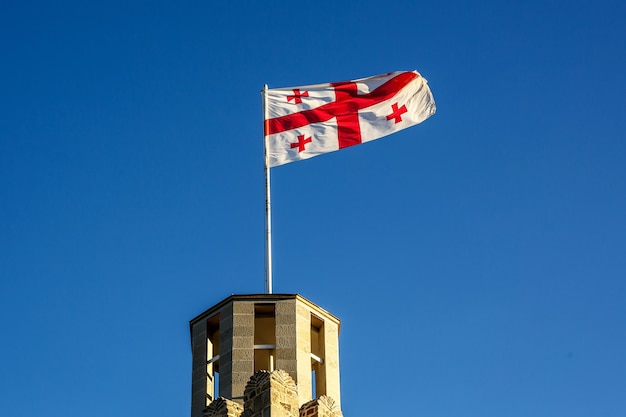 The Georgia flag on the roof of an ancient tower against the clear blue sky