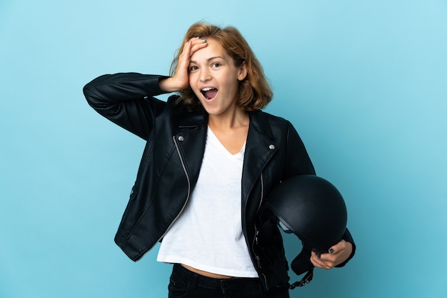 Georgian girl holding a motorcycle helmet isolated on blue wall with surprise expression