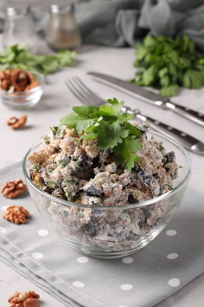 Georgian salad with eggplant and walnuts in a transparent bowl on a light gray background. Traditional appetizer of Georgian cuisine