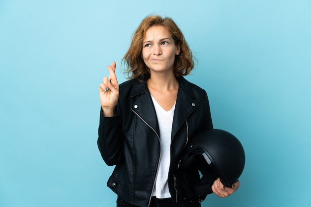 Georgisch meisje dat een motorhelm houdt die op blauwe achtergrond met vingers wordt geïsoleerd die en het beste wensen