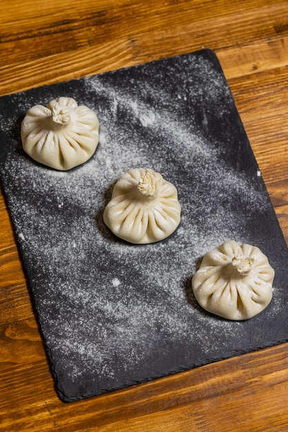 Georgische dumplings khinkali met vlees op een houten bord met bloem zwarte achtergrond proces van makin...