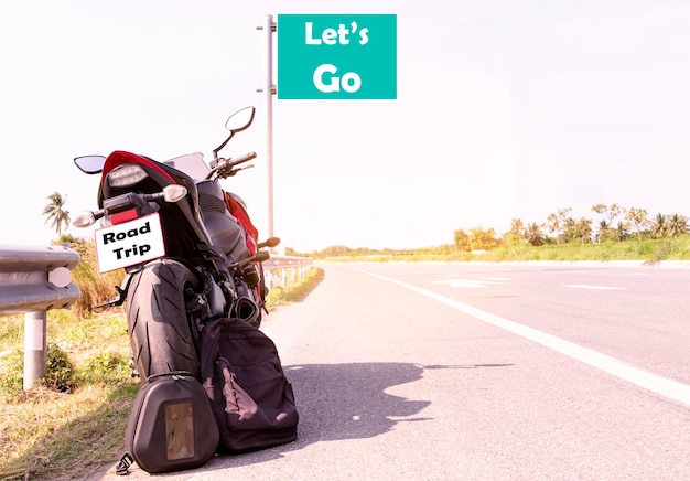 Geparkeerde motorfiets en zwarte rugzak met bericht Let's go on green bord op snelwegwegzicht