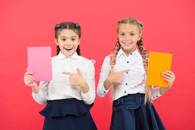 Gepassioneerd door boeken Gelukkige kleine meisjes wijzend op boeken op rode achtergrond Schattige kleine kinderen lachend met encyclopedie of handboeken Educatieve boeken voor leerlingen en studenten